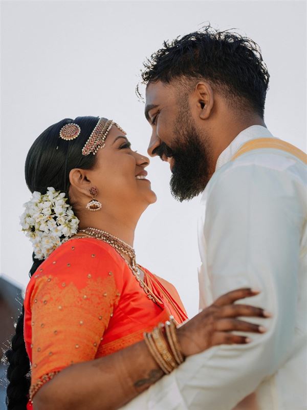 Tamil bride and groom smiling at each other against a bright sky